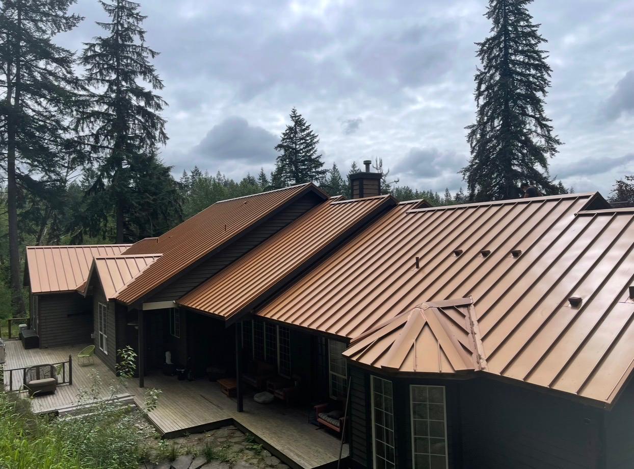 Copper-finish standing seam metal roof on a home surrounded by fir trees in the Greater Eastside, WA