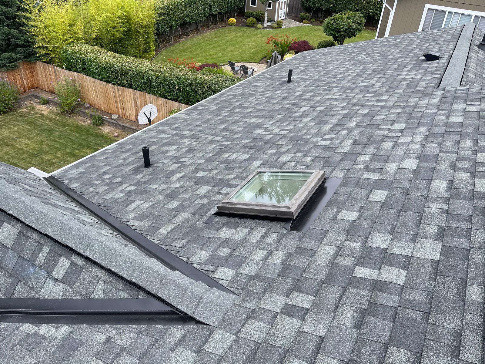 Architectural shingle roof with a flashed skylight above a landscaped back garden in the Greater Eastside, WA