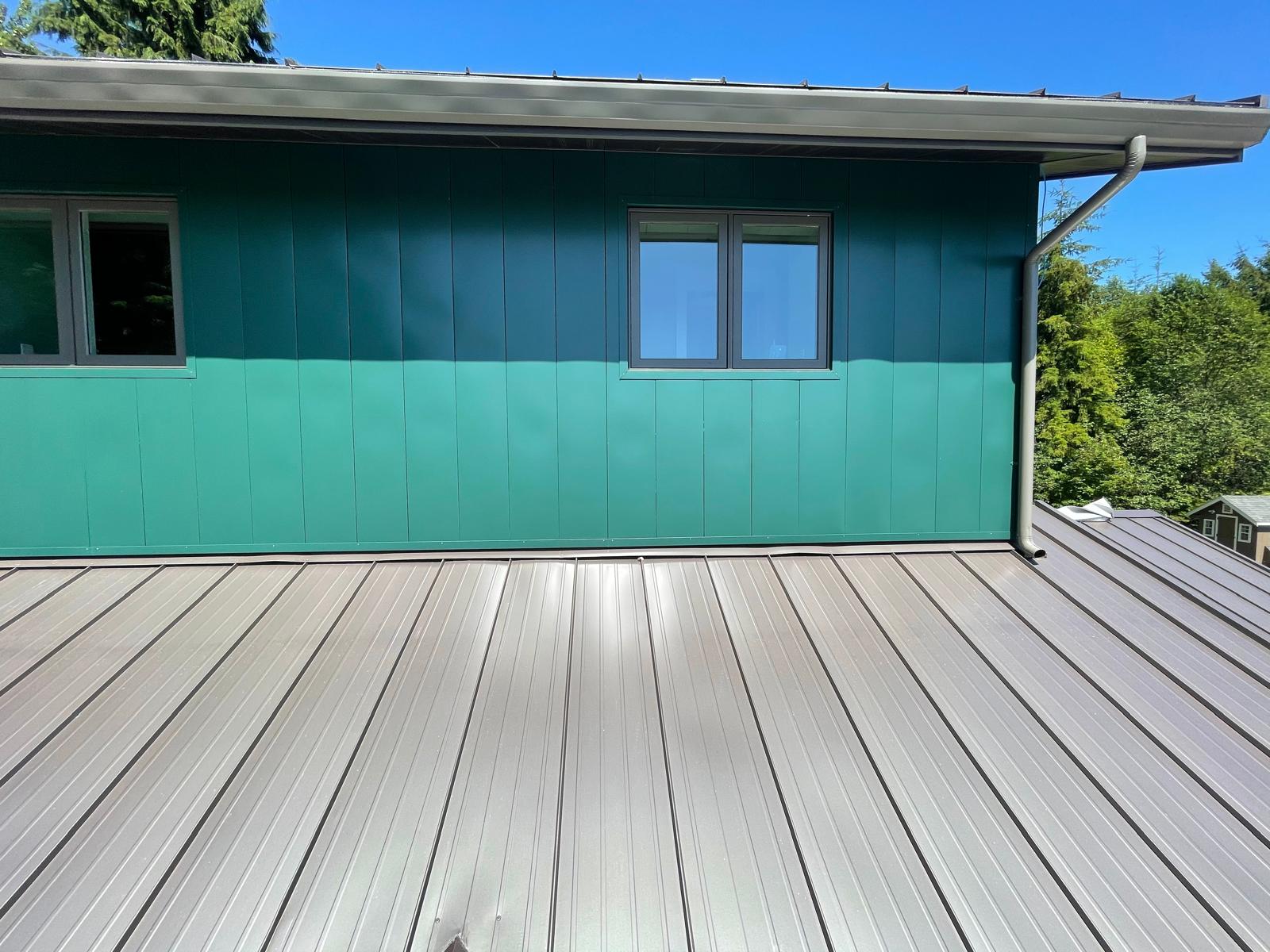 Low-slope standing seam metal roof meeting an exterior wall, with gutter and downspout