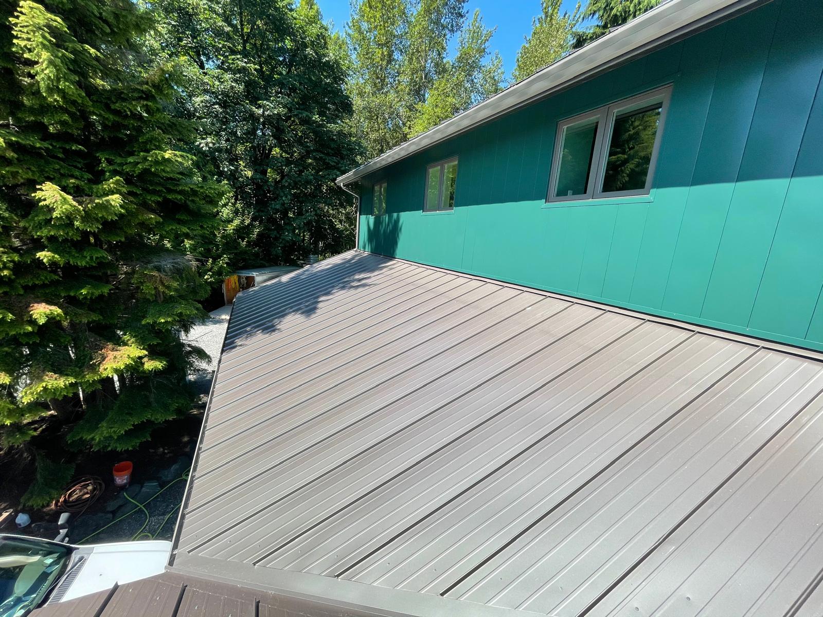 Bronze standing seam metal roof over a low-slope addition beside teal board-and-batten siding in the Greater Eastside, WA