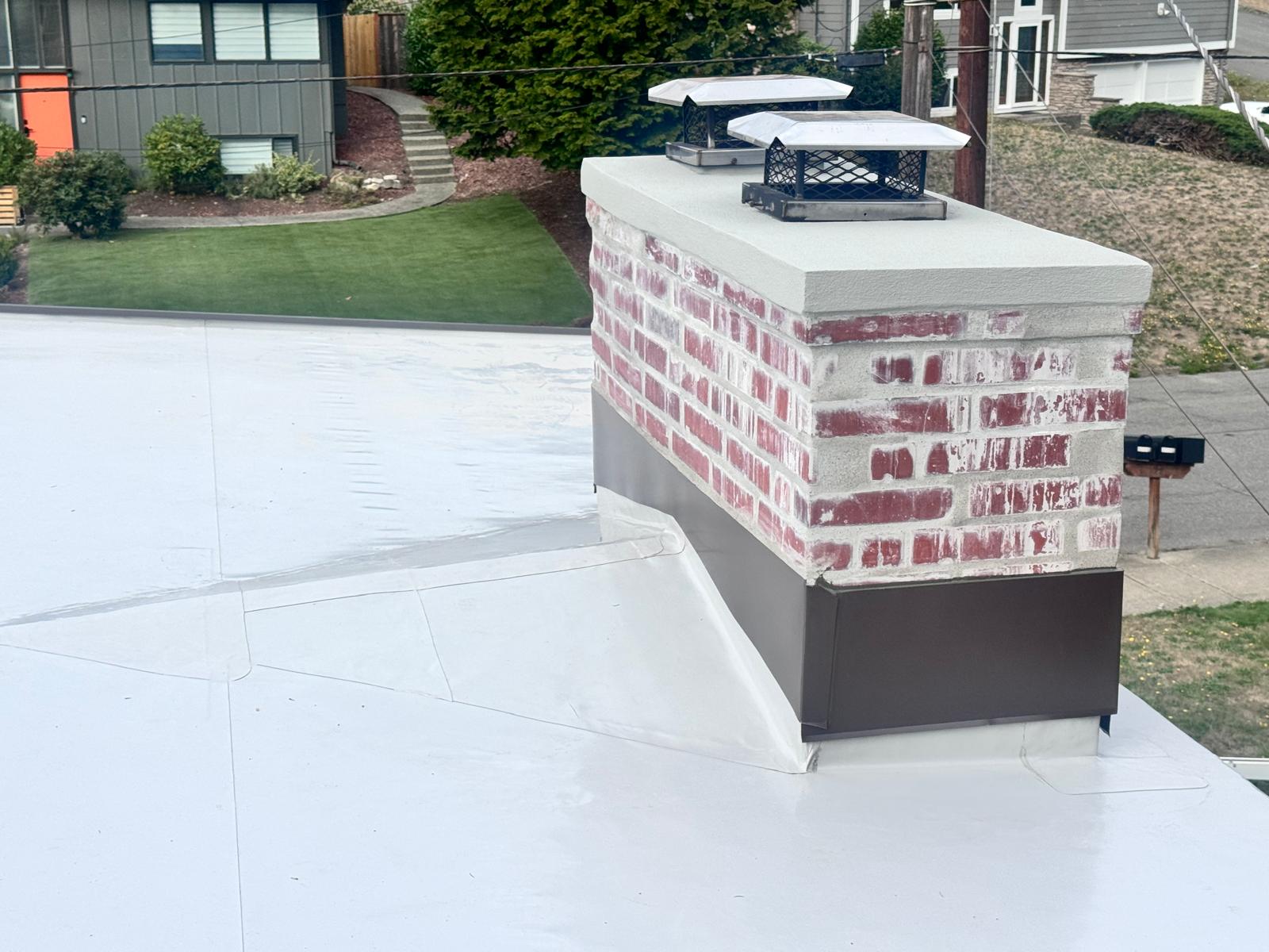 Brick chimney with new metal flashing on a new white PVC membrane roof